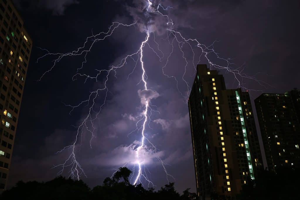 Un éclair frappe entre des immeubles de grande hauteur la nuit, illuminant le ciel de ses branches ramifiées – un rappel brutal de l’importance d'installer un paratonnerre.