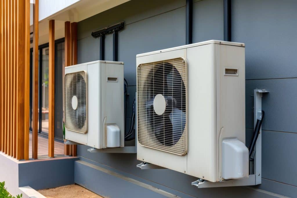 Deux unités de climatisation extérieures sont montées côte à côte sur le mur extérieur d'un bâtiment moderne, mettant en évidence les solutions d'efficacité énergétique et les considérations telles que le prix pompe à chaleur.
