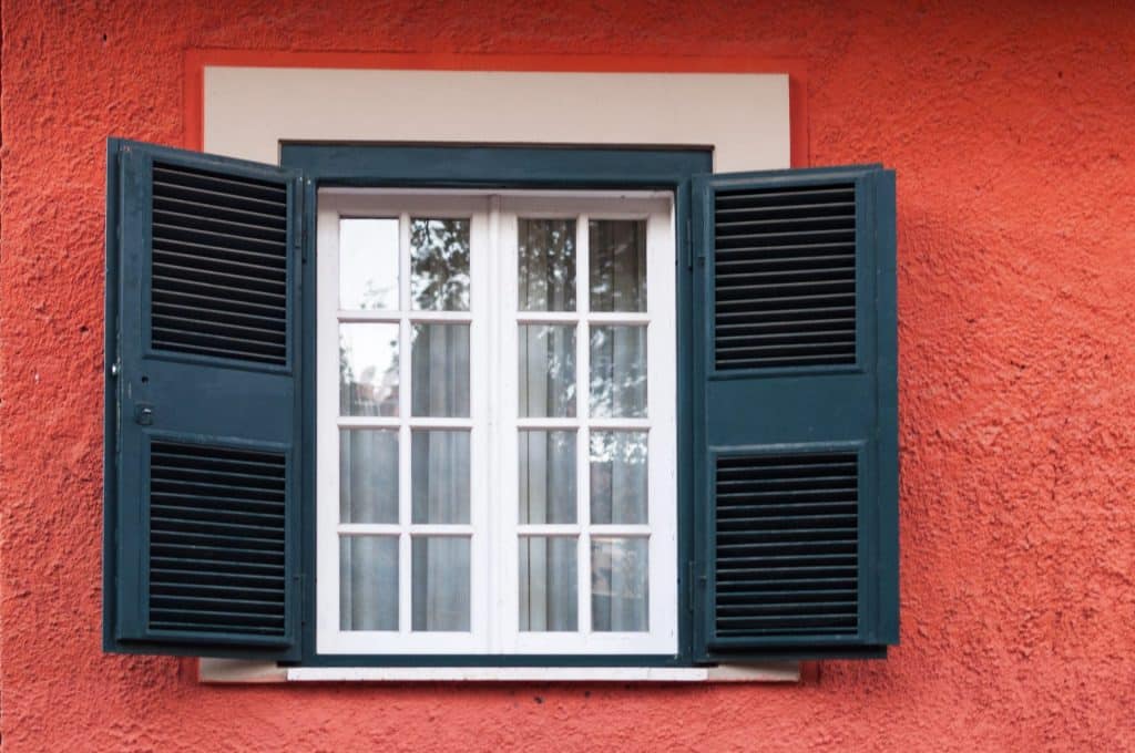 Une fenêtre à cadre blanc avec des vitres et des volets noirs est ouverte sur un mur orange texturé, mettant en valeur une rénovation de fenêtres élégante.